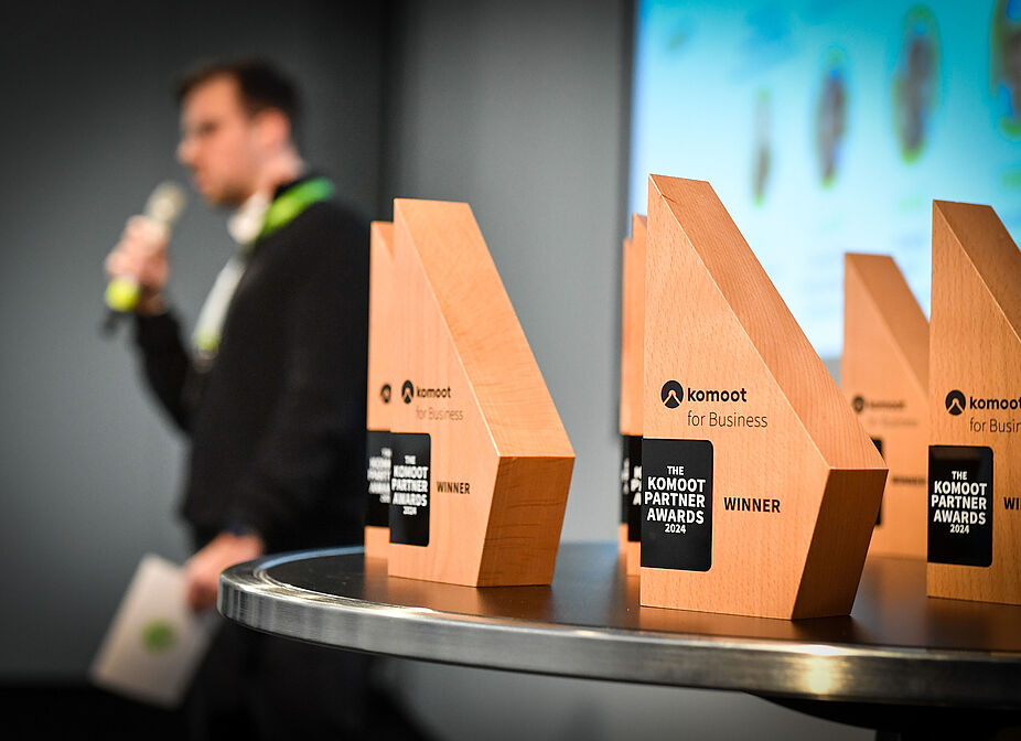2025_komoot_Partner_Awards_2024_Gabriele-Griessenboeck Awardauszeichnungen der komoot Parner Awards 2024 im Vordergrund, im Hintergrund verschwommen ein Redner