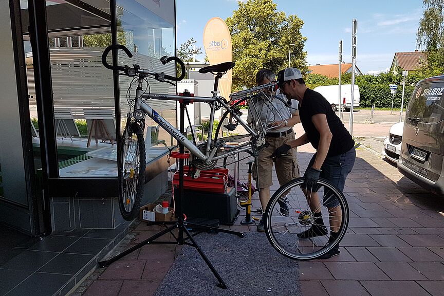 WorkshopParksiedlung 2 Menschen stehen vor einem Fahrrad das in einem Reparaturständer hängt