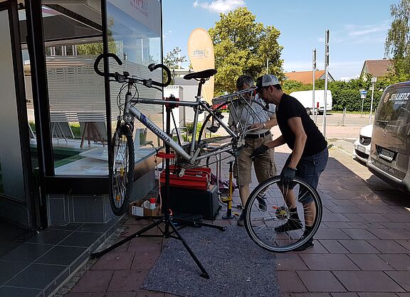 2 Menschen stehen vor einem Fahrrad das in einem Reparaturständer hängt