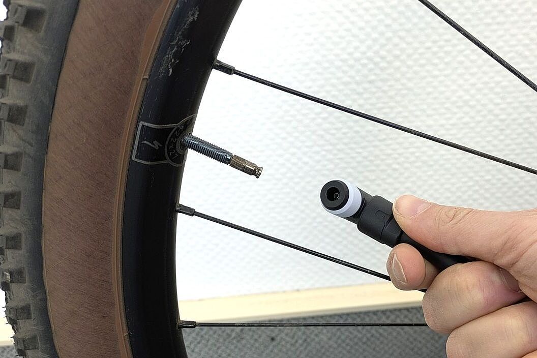 Großaufnahme des neuen Fahrradventils Clikvalve in eiem MTB-Laufrad mit danebengehaltenem Pumpenkopf. 