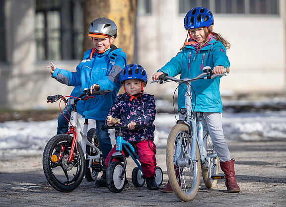 Drei Kinder in unterschiedlichem Alter auf Fahrrädern.