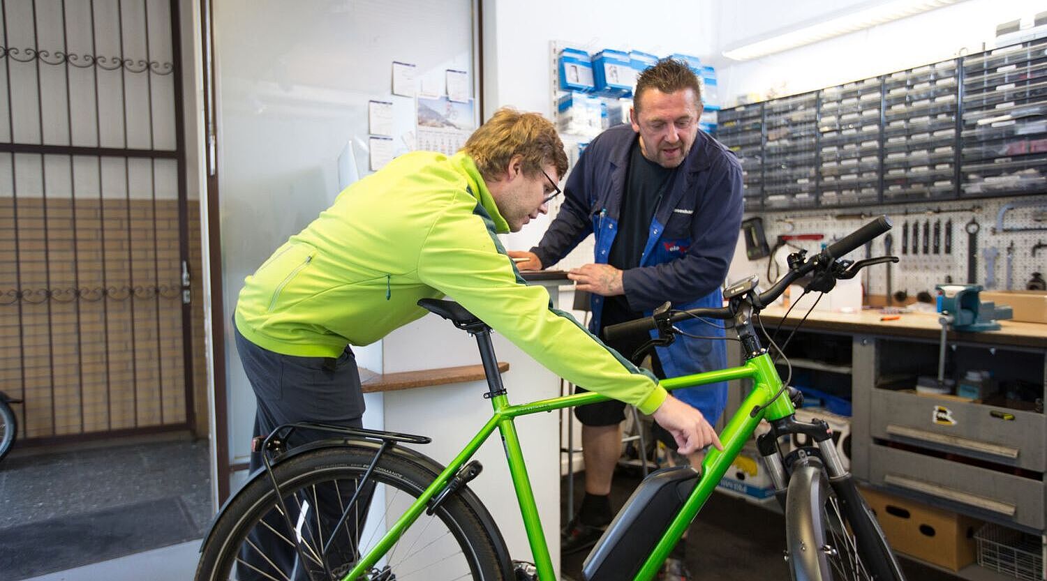 Ein Kunde zeigt dem Mechaniker in einer Werkstatt einen Defekt am Rad. 