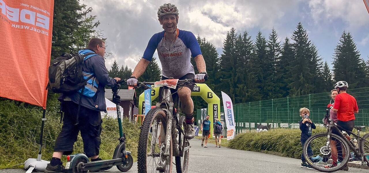 happy im ziel Ein mit schlamm bespritzter Mountainbiker hat gerade einen Zielbogen passiert und lächelt.