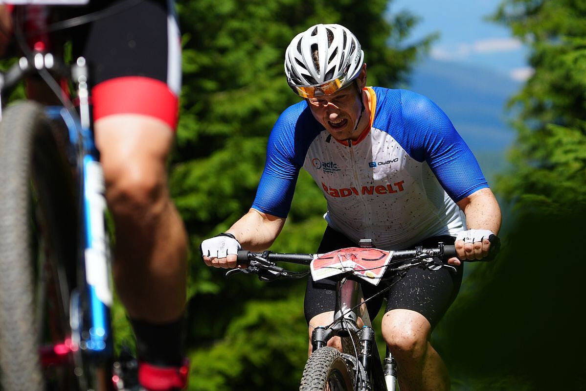 Leidenszeit Ein Mountainbiker fährt mit schmerzverzerrtem Gesicht einen Anstieg hinauf.