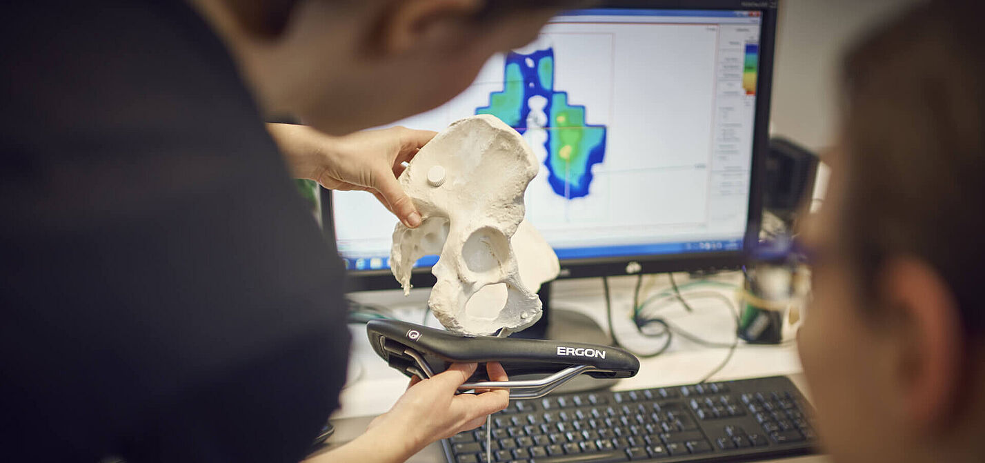 Ergonomischer Sattel Eine Person hält ein Modell eines Beckens auf einen Fahrradsattel. Das Foto veranschaulicht die Analyse der Ergonomie zwischen menschlicher Anatomie und Fahrradsitz.