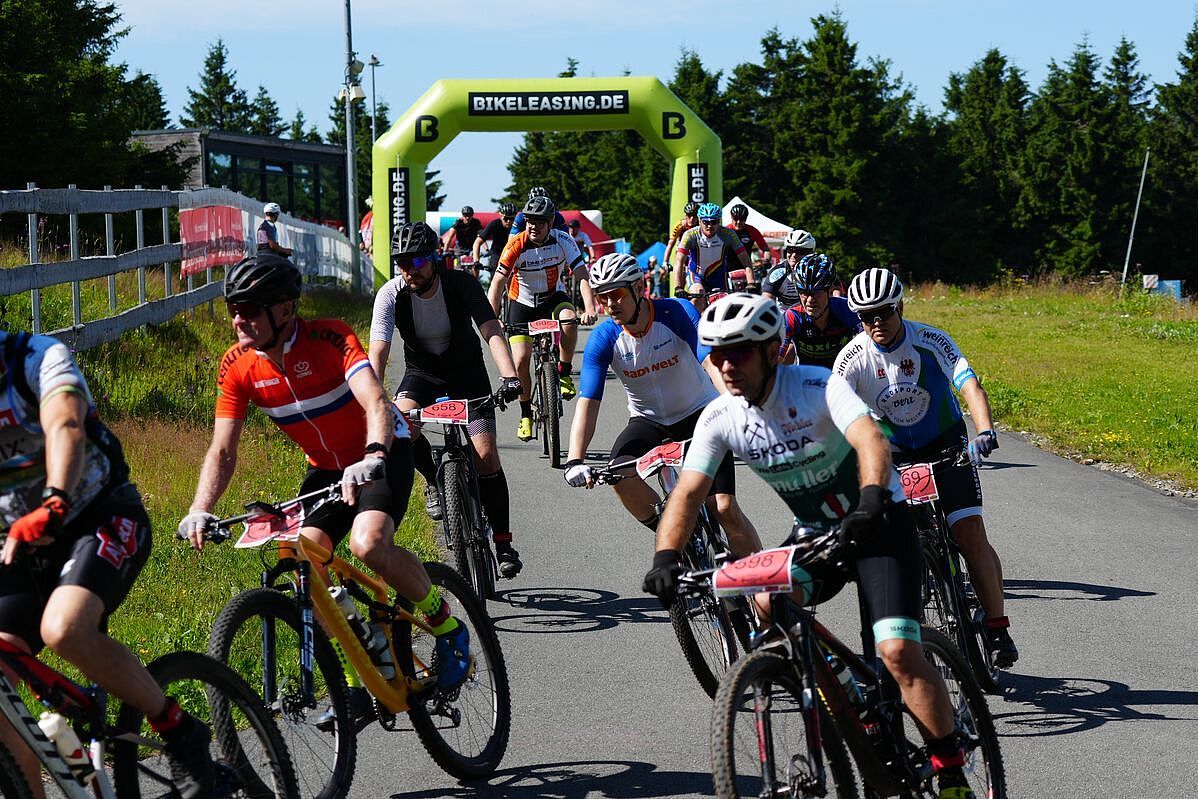 Start zum erzgebirgsradrennen Eine Menge Mountainbiker startet zu einem Wettkampf bei Sonnenschein. Im Hintergrund ist ein Startbogen zu sehen.