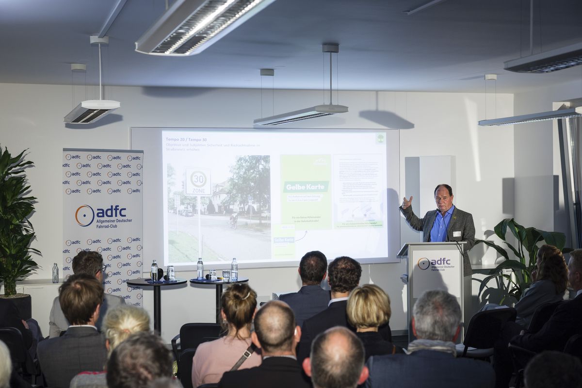 Jörg Jenoch, Bürgermeister der Gemeinde Eichwalde, am Podium, hinter ihm die Leinwand mit einer projizierten Präsentation. 